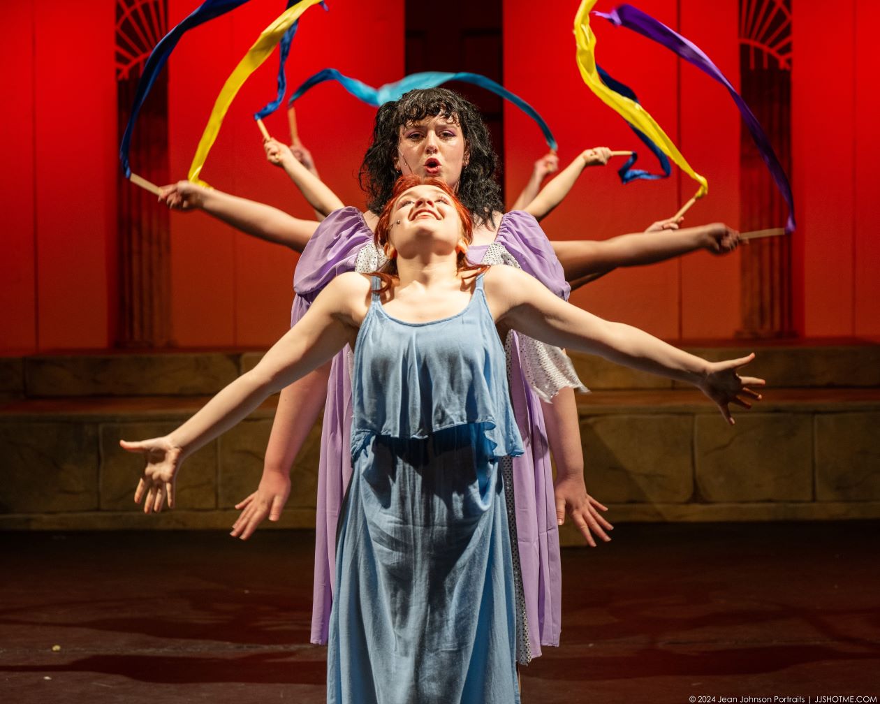 Two performers singing with ensemble dancers and ribbons in a choreographed stage scene